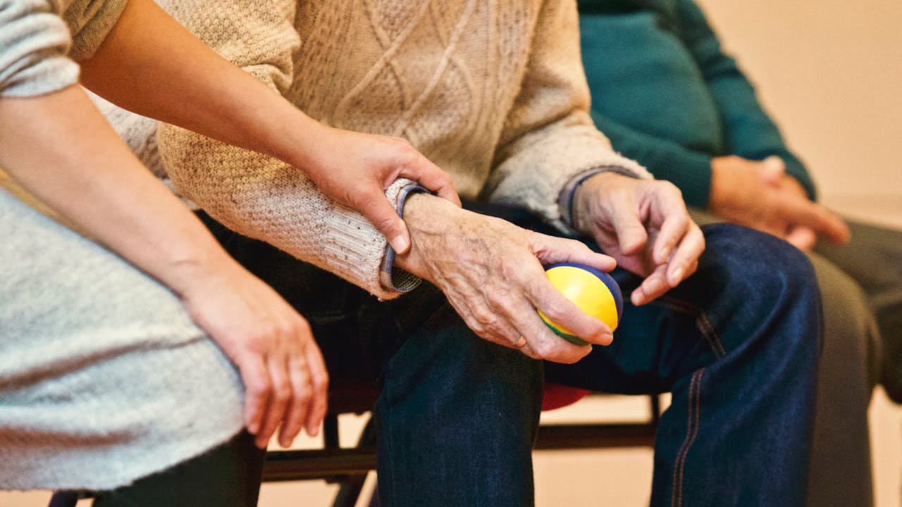 who-we-are An elderly person receives support from a caregiver, holding hands indoors, showcasing compassion.