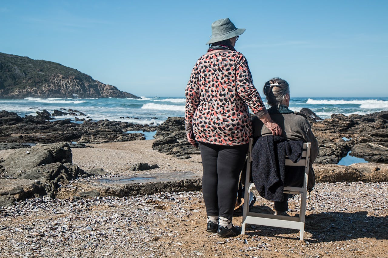 services-05 Two senior women enjoying a peaceful moment by the rocky beach, embracing friendship and serenity.